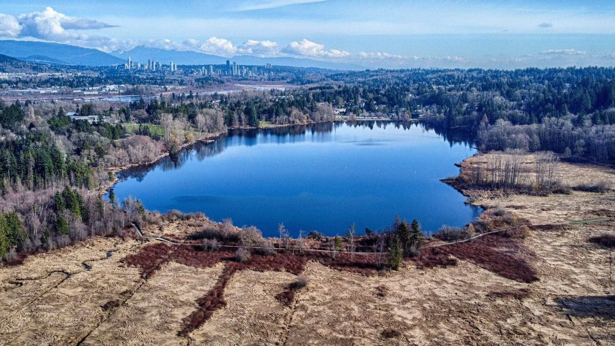 View across Deer Lake in Burnaby with the calm lake surface reflecting the surrounding forested shoreline.