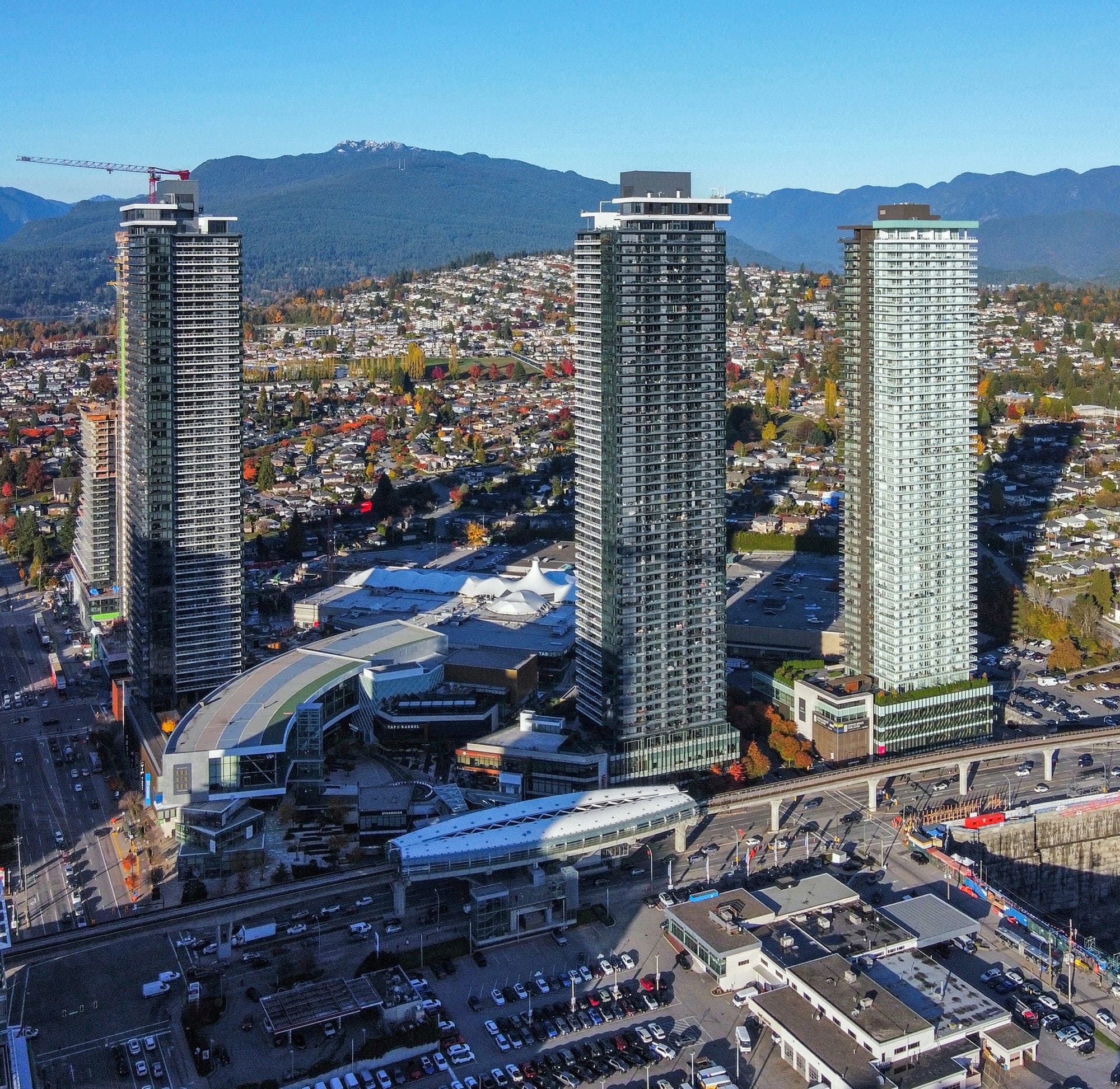 The Amazing Brentwood development in Burnaby, showing several new residential towers surrounding a central open-air plaza and the Millennium Line SkyTrain station.