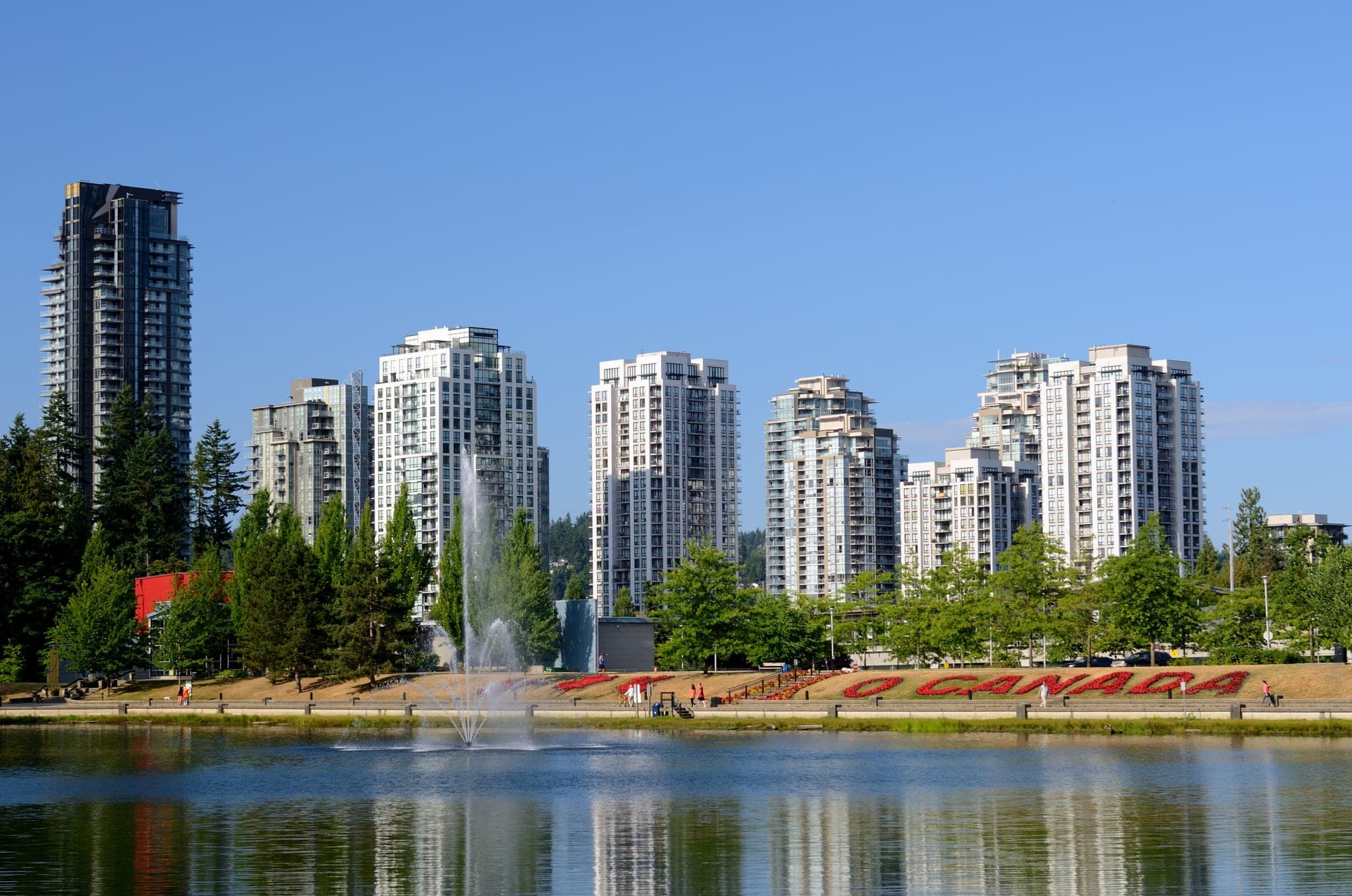 Lafarge Lake in Coquitlam City Centre, with the calm water surface reflecting surrounding trees and new residential high-rise towers.