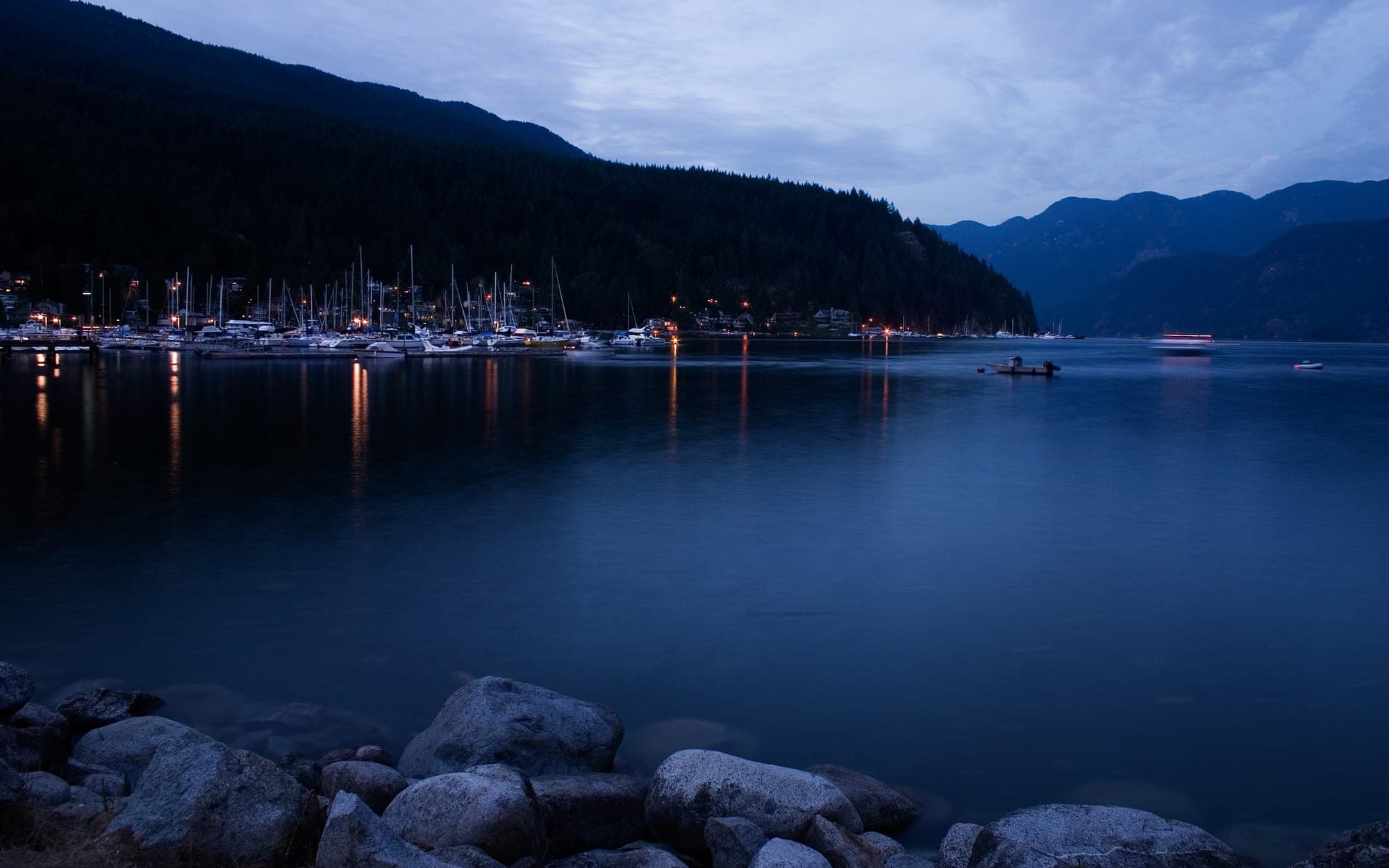 The beach and calm waters at Deep Cove in North Vancouver, with kayaks drawn up on the sand and forested hillsides surrounding the fjord.