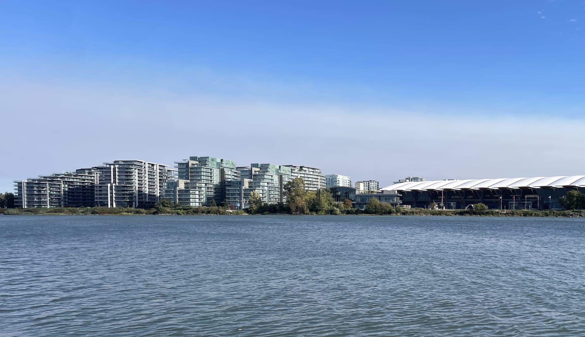 The Richmond Olympic Oval and surrounding waterfront district on the Middle Arm of the Fraser River, with mountains in the background.