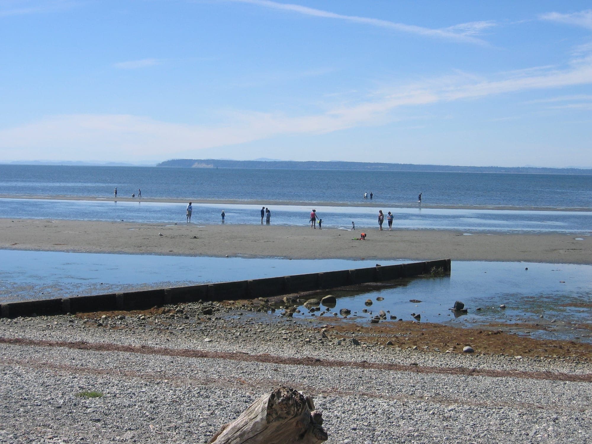 A stone groyne extending into the calm waters of Boundary Bay at Crescent Beach, Surrey, with mountains visible across the water.